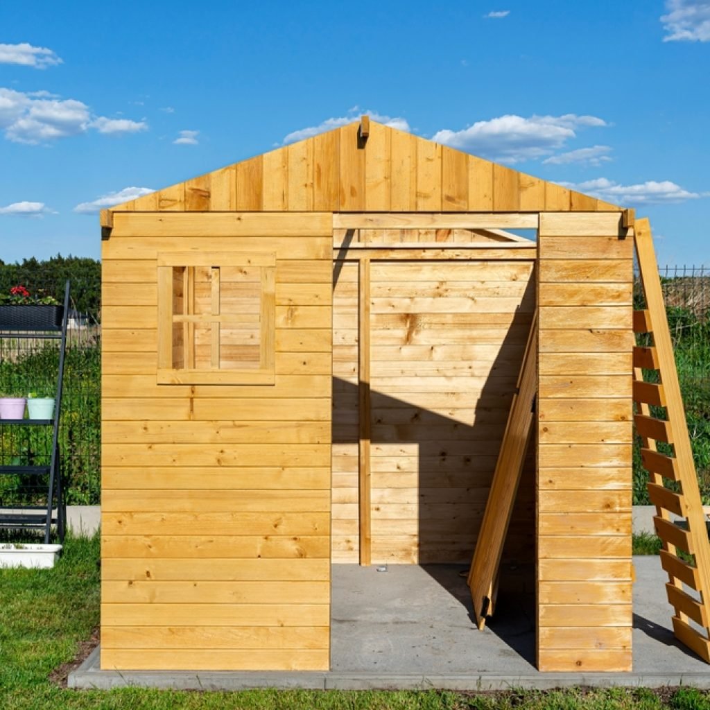 A partially constructed wooden backyard shed on top of a solid concrete foundation. 