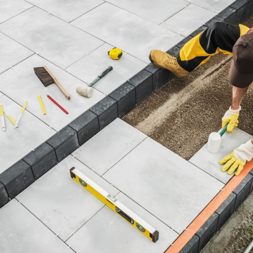 A DIY person hammering in tiles to a foundation with various work tools around them.
