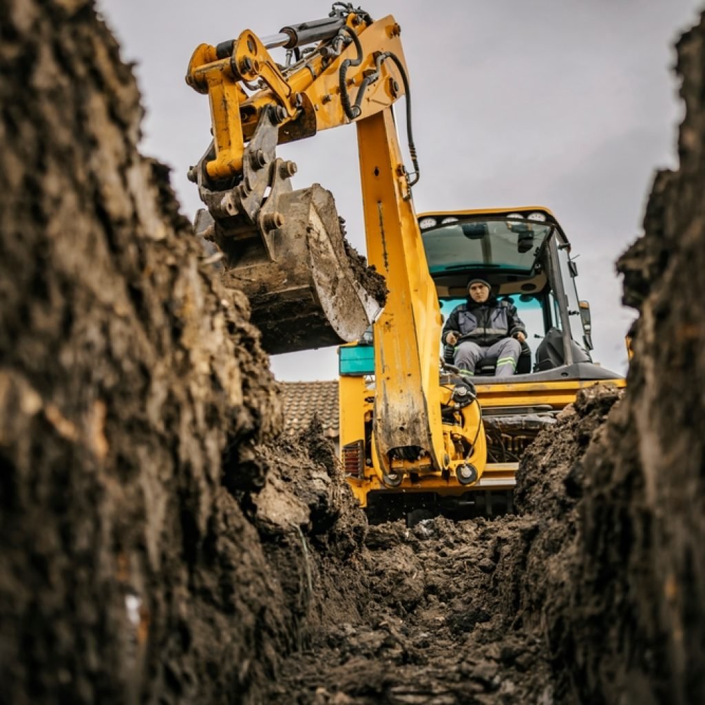 An ant's view within a hole looking up at an man operating an excavator.