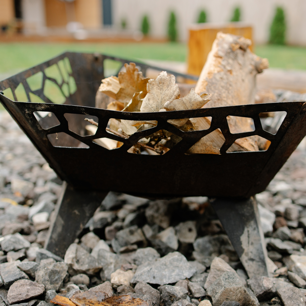 A modern black metal fire pit filled with logs sits on a professional base of crushed grey river stones.